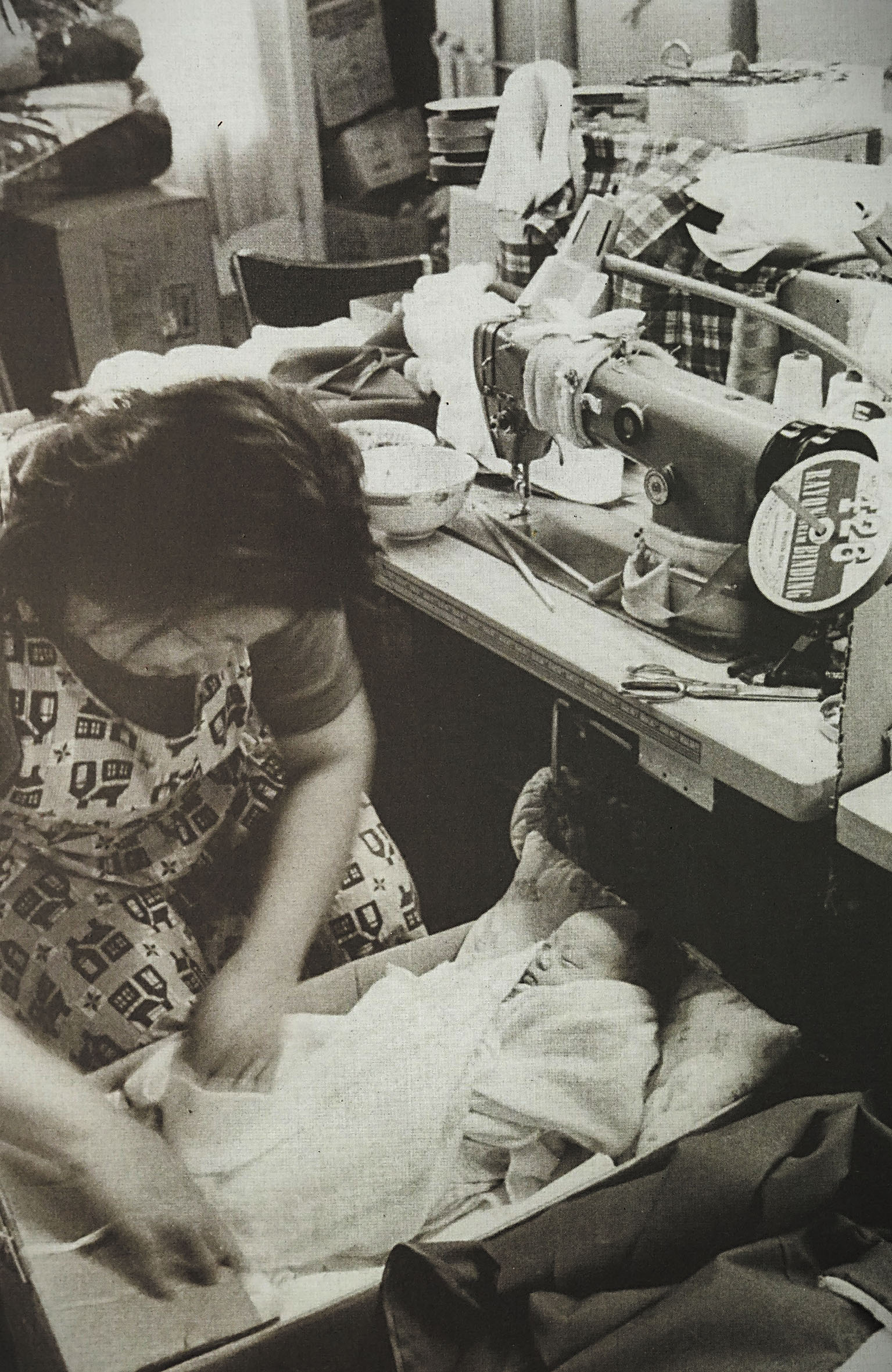 1977年,一名車衣女工在工廠的衣車旁進餐時抽空照顧滿月的嬰兒。CHSA