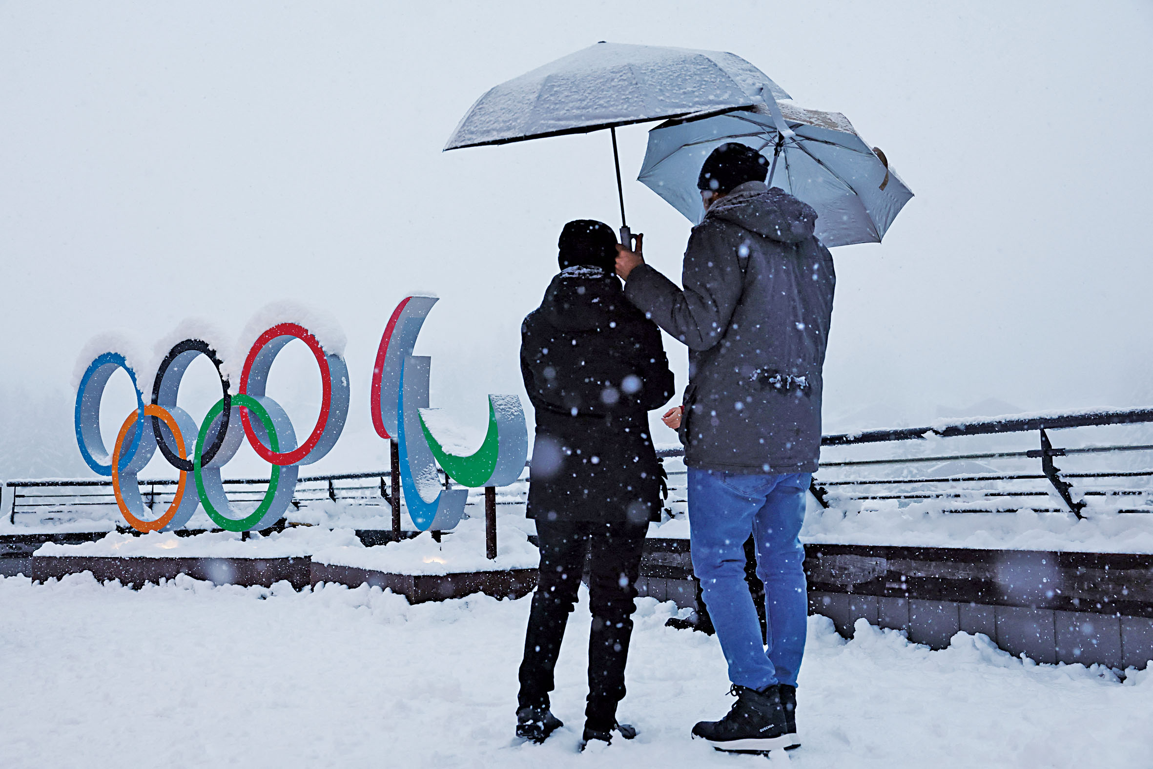 人們撐著傘冒雪站在科爾蒂納丹佩佐的奧運五環標誌旁。路透社