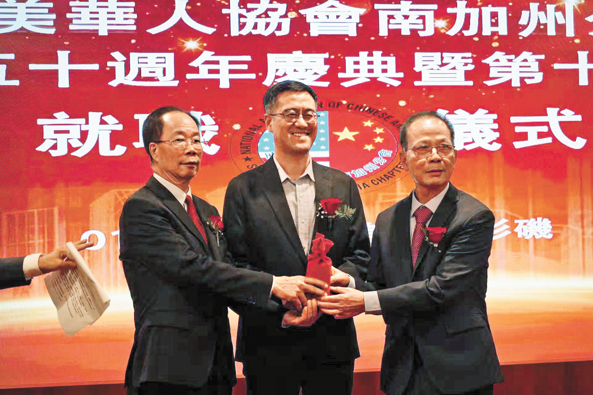 關健榮會長（左）將會務交接給新任會長何暢源，中為郭志強副總領事。本報記者攝