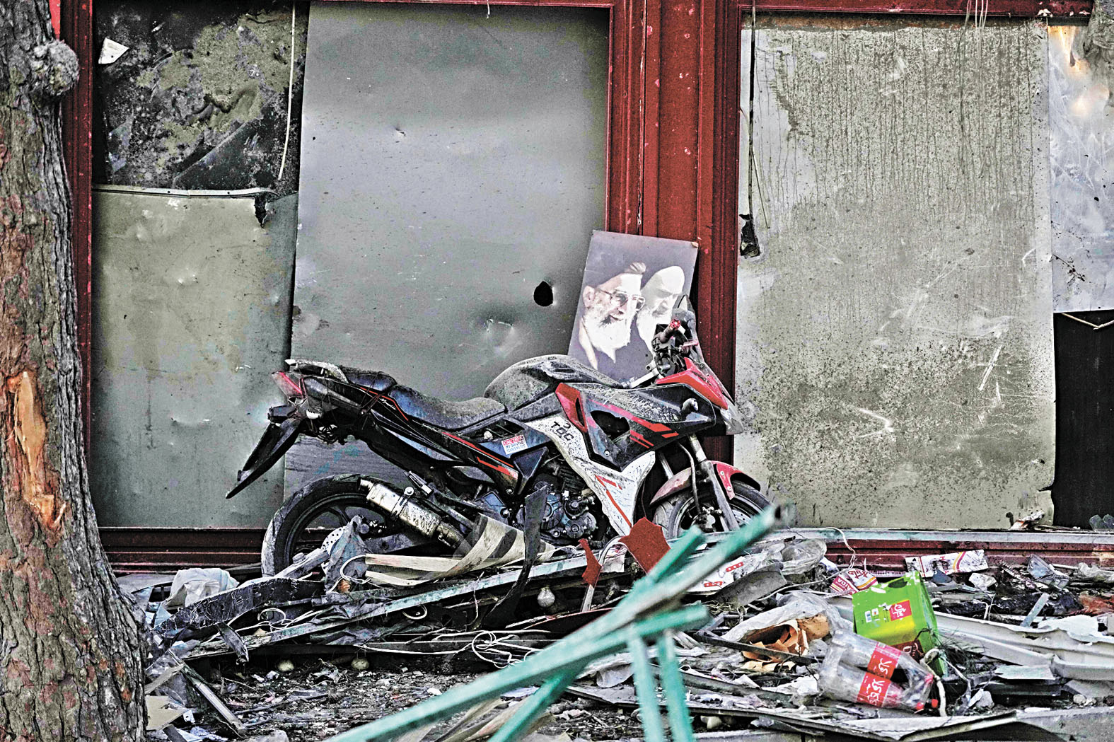 在伊朗德黑蘭，一輛摩托車上散落著伊朗最高領袖哈梅內伊（在美以聯合軍事行動中喪生）和伊朗革命創始人霍梅尼（右）的畫像，摩托車周圍是空襲留下的廢墟。 美聯社