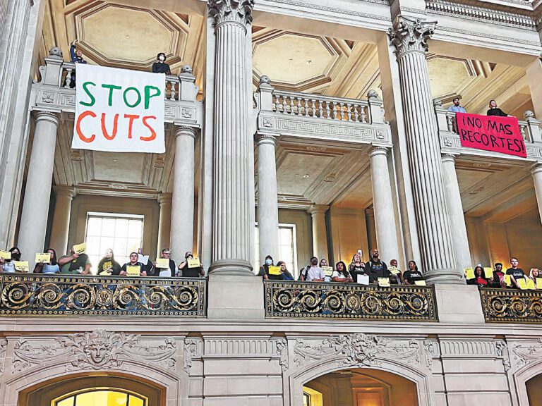 三藩市市長羅偉計劃削支裁員，圖為去年6月市府預算協商期間工會代表在市參事會上舉標語呼籲不要削減。本報資料圖片，記者陳程威攝