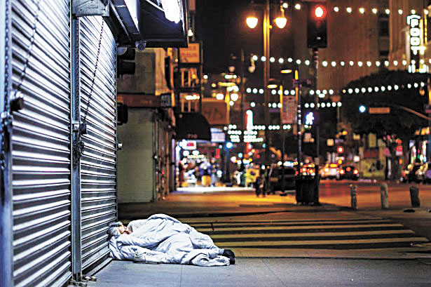 一名無家可歸的女子蜷縮在洛杉磯市區人行道上，蓋著一條棉被。洛杉磯時報