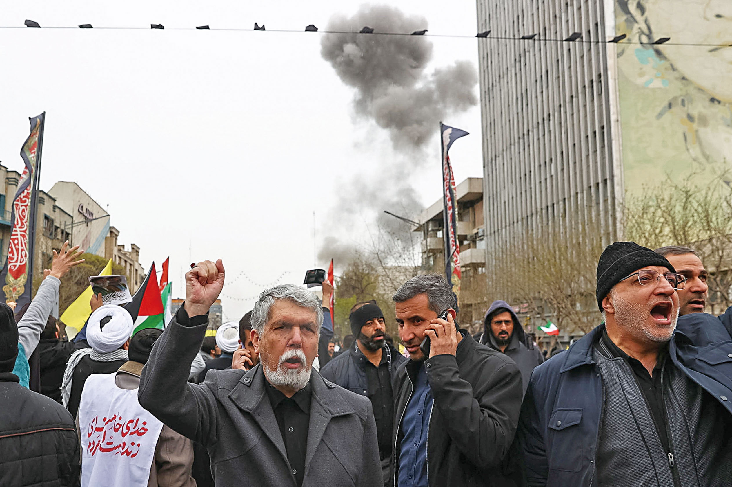 人們13日在德黑蘭參加集會，現場轟炸不斷，黑煙滾滾。路透社