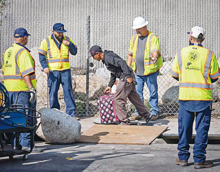 當工人準備焊接井蓋時，一名男子提著行李箱從下水井爬出。 洛杉磯時報