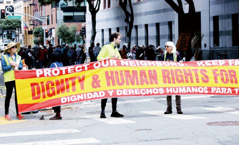 示威者在ICE辦公室所在街道組成人牆封路，舉起「人人享有尊嚴與人權：驅逐ICE」大型橫幅。記者陳程威攝