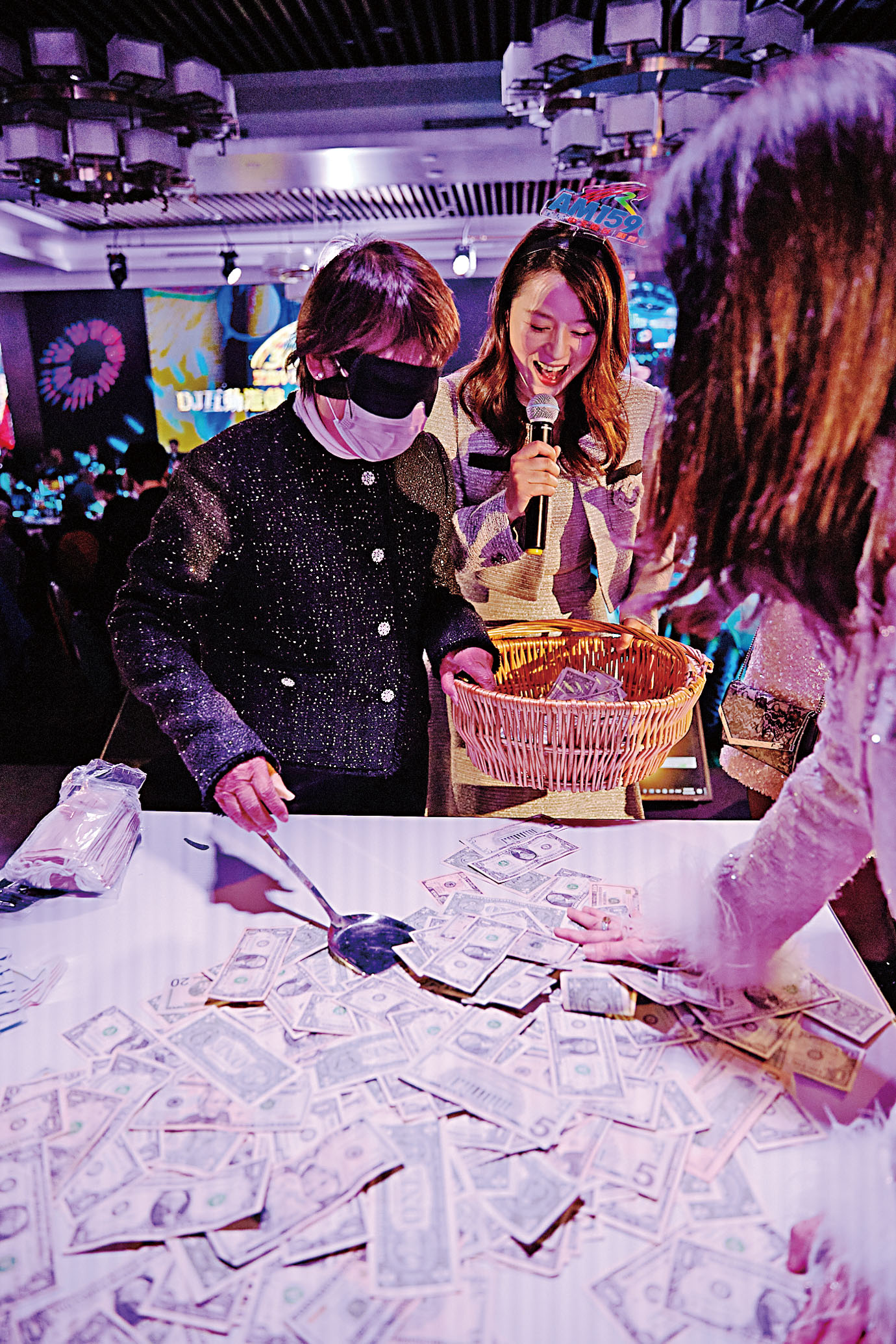 星島電台DJ粉絲團「鏟錢」遊戲，嘉賓蒙眼用鍋鏟將桌上1-100元面額不等的現金鏟入籃中。