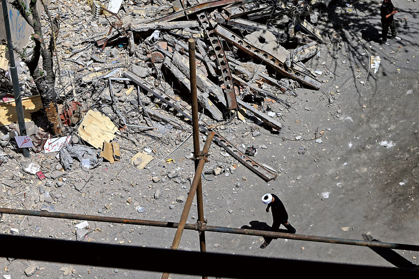 伊朗戰事持續衝擊全球經濟。圖為伊朗德黑蘭一名神職人員走過受損的居民樓。路透社