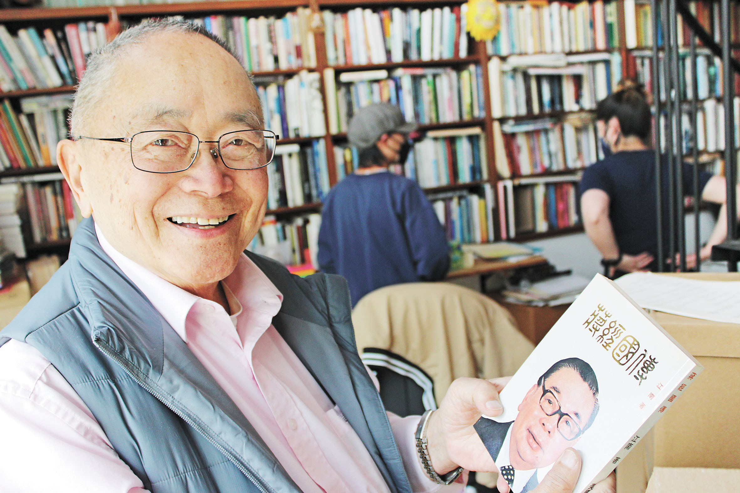 王靈智在三藩市寓所接受本報專訪，身後書架藏書滿盈，他手持的是「蔣經國傳」。記者陳程威攝