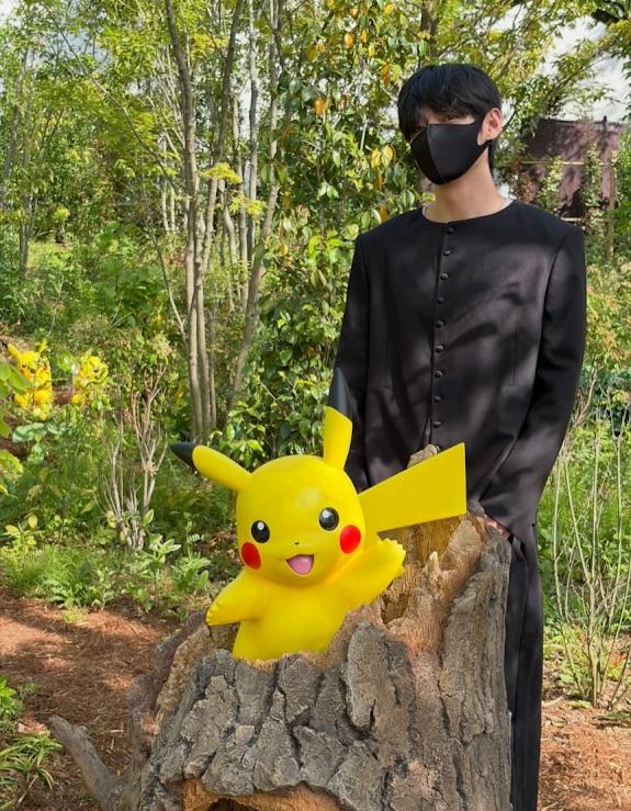 V戴著黑色口罩，在比卡超旁邊拍照留念。