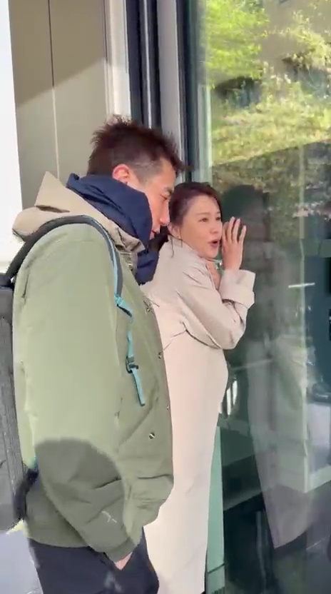 面對強風，兩人緊貼牆壁躲避，表情趣怪。