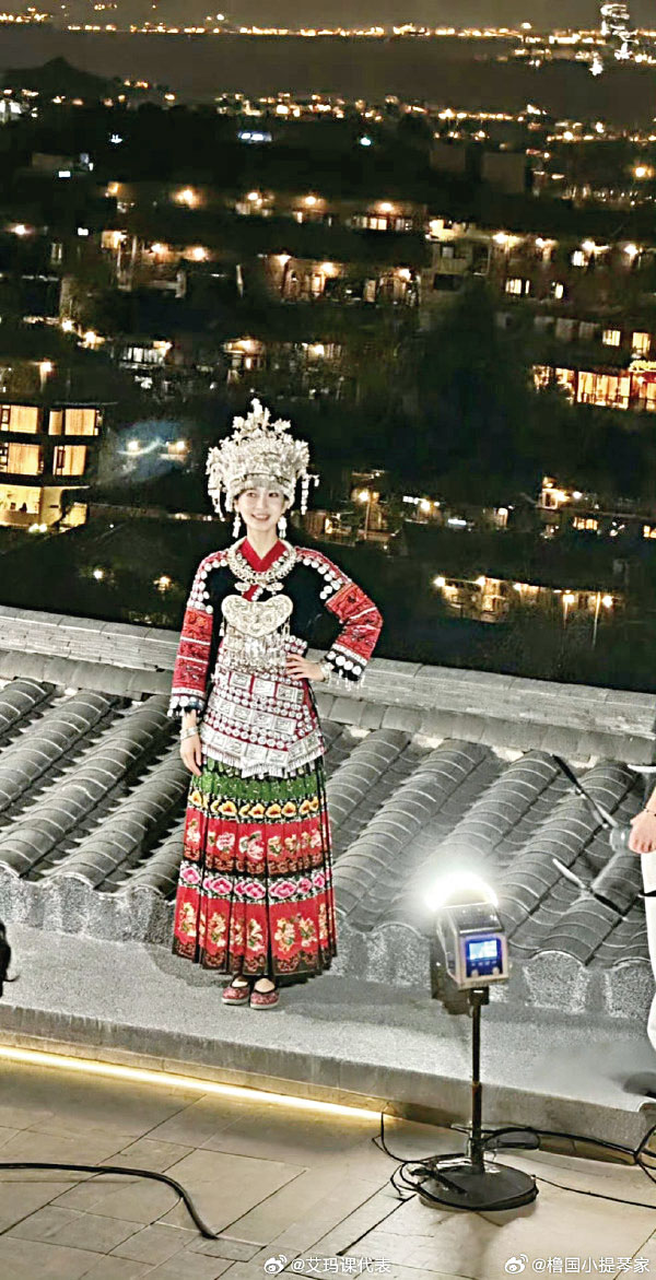 她身穿刺繡服飾，站在吊腳樓背景下，畫面格外和諧。網上圖片