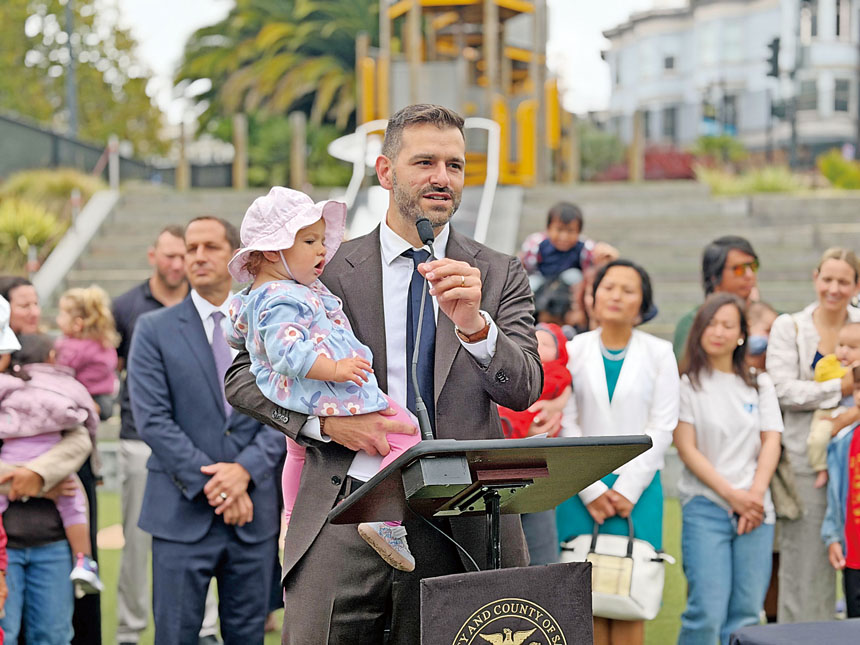 第3區市參事李爾德抱著年幼女兒出席法案簽署儀式。他表示，身為新手父親，深切體會在三藩市養育孩子的喜悅與挑戰。記者蘇婕雅攝