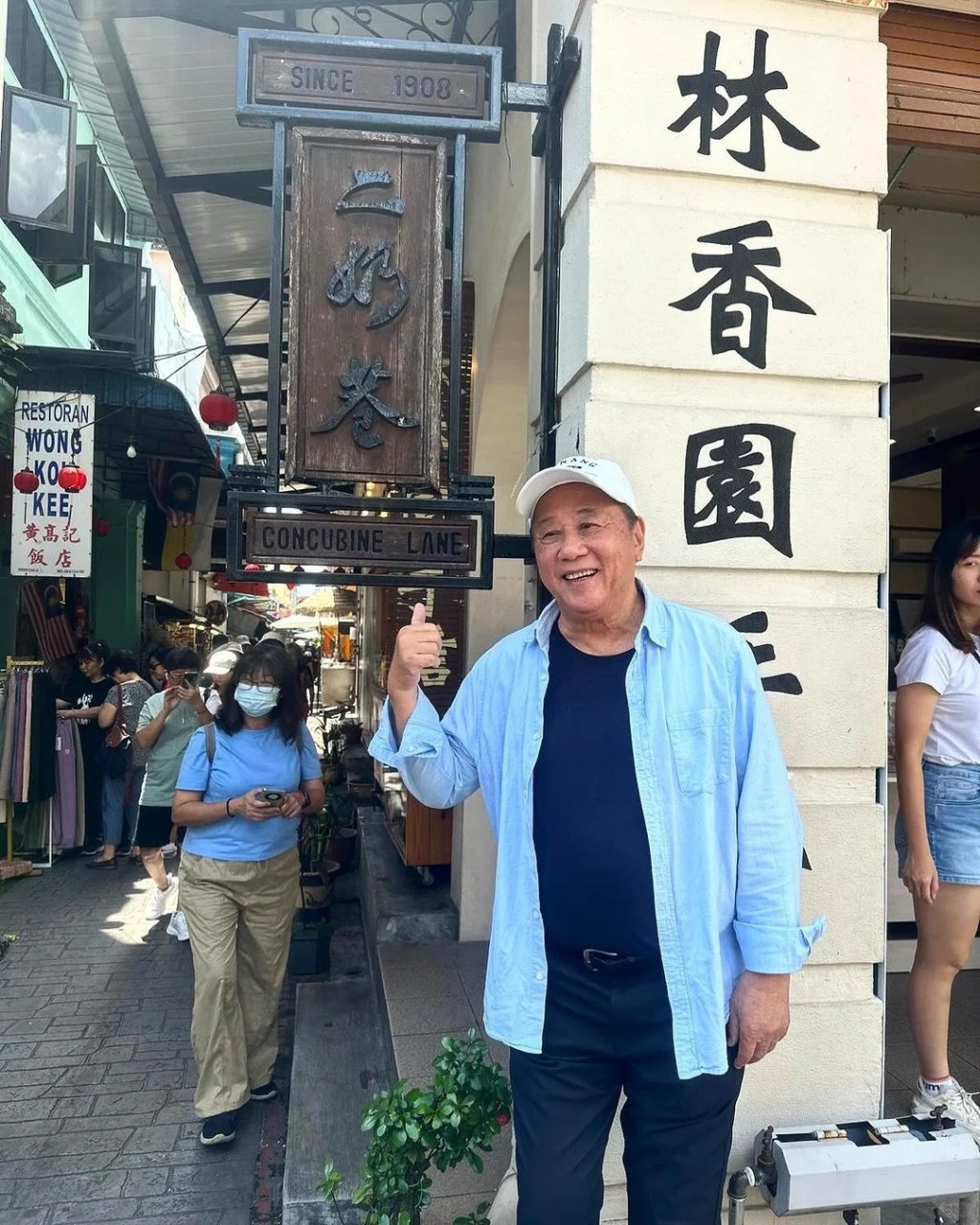 照片中，夏雨穿上淺藍色襯衫配深藍色T恤，戴上白色cap帽，在馬來西亞著名景點怡保二奶巷的牌匾及壁畫前留影。
