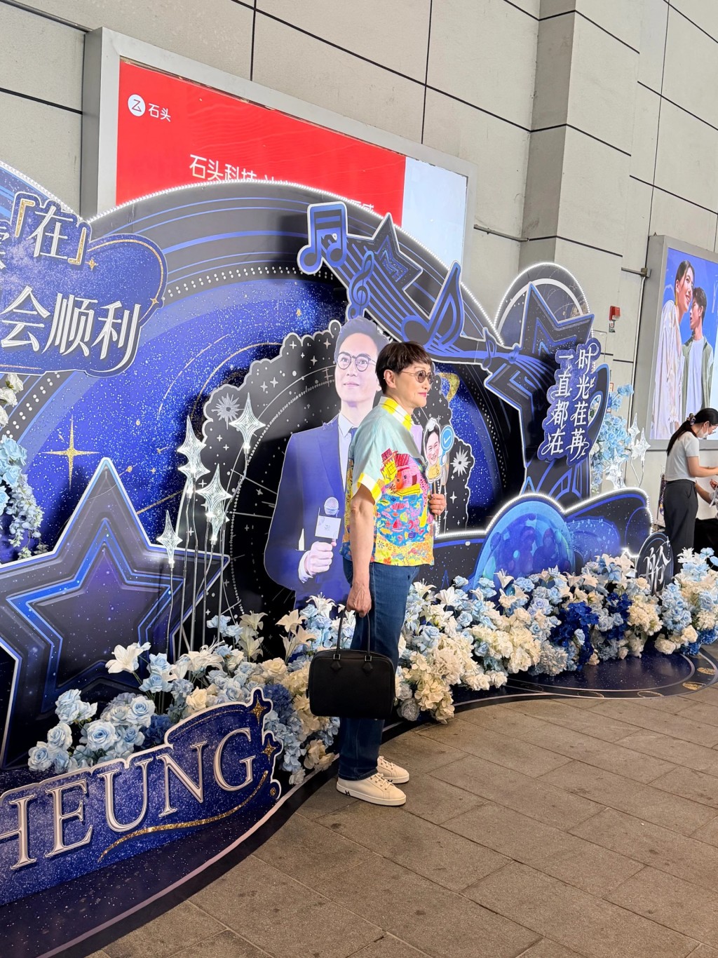 張智霖母親在入場前,於演唱會佈景板前拍照留念。