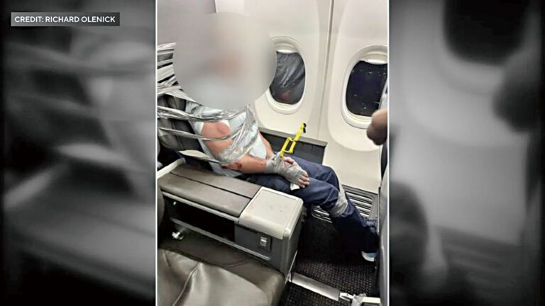 男子遭其他乘客及機組人員以膠帶及束線帶綑綁於座位上。CBS紐約截圖