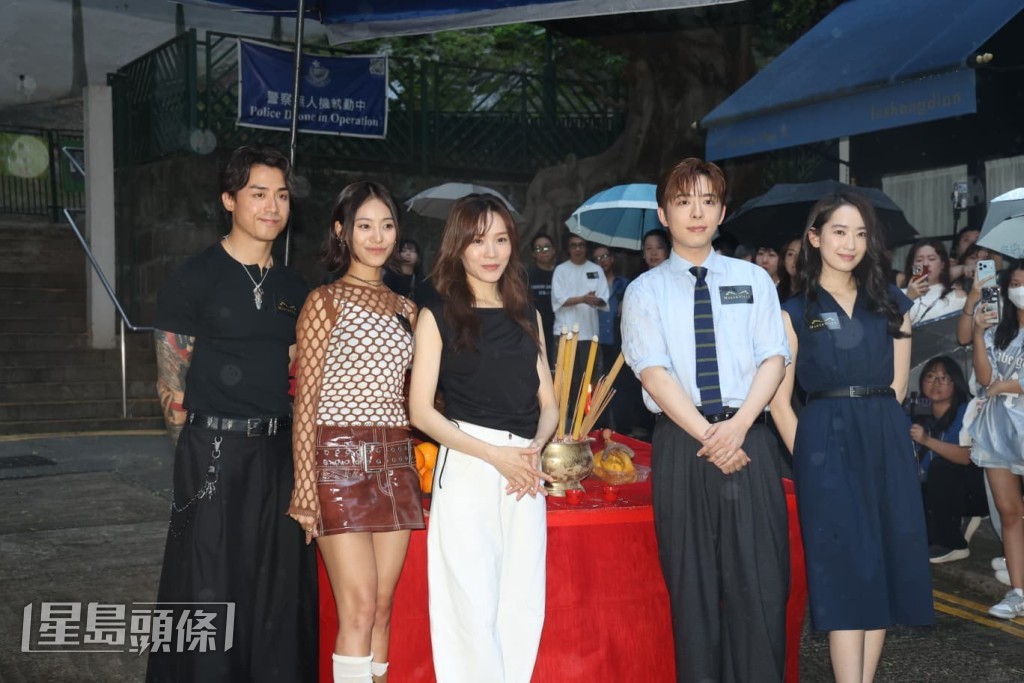 由於帳篷空間有限，五位演員需在雨中拍攝大合照。