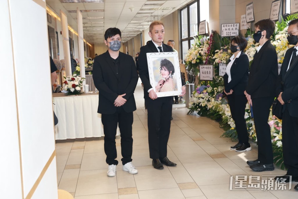 李泳漢手捧母親施明的遺照步出靈堂。