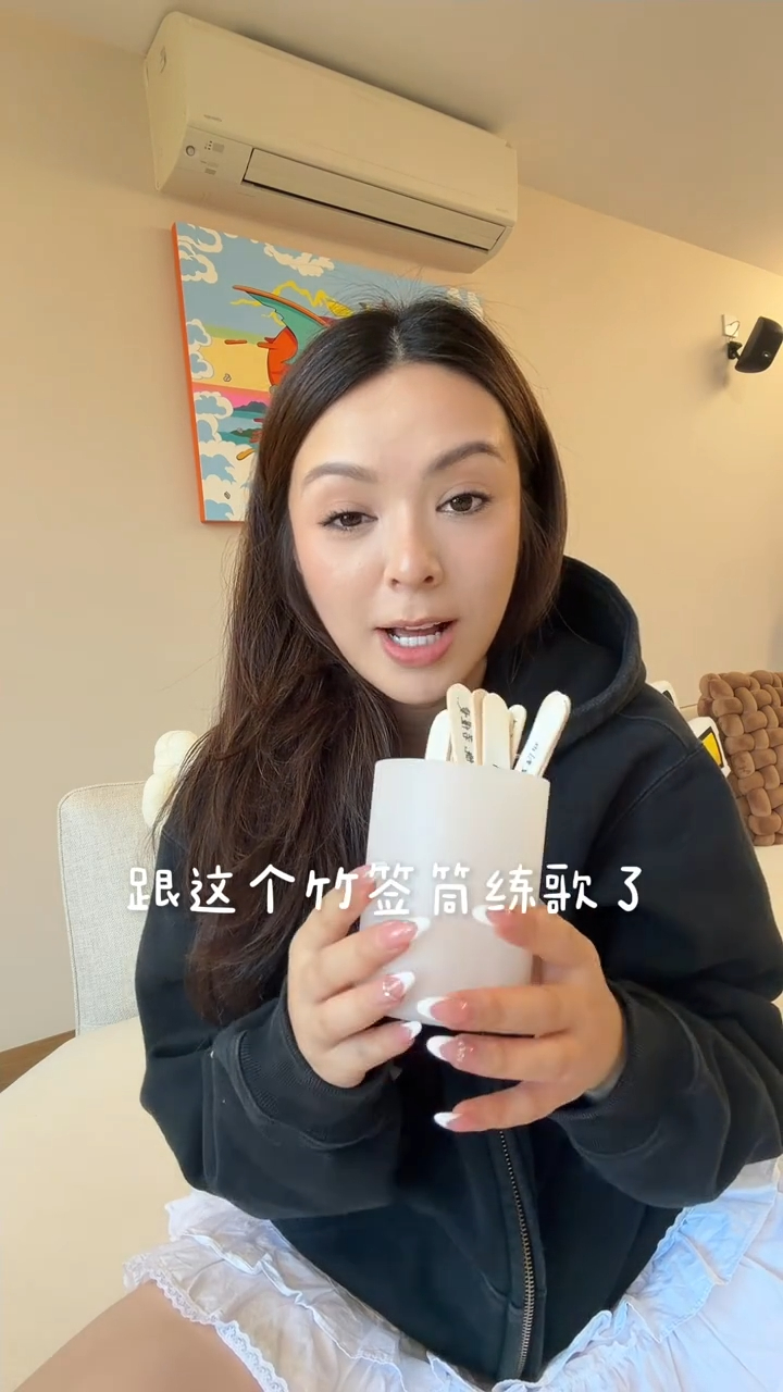 JW王灝兒手拿寫滿歌名的竹籤筒,身後的米白色梳化與掛畫展現簡約品味。