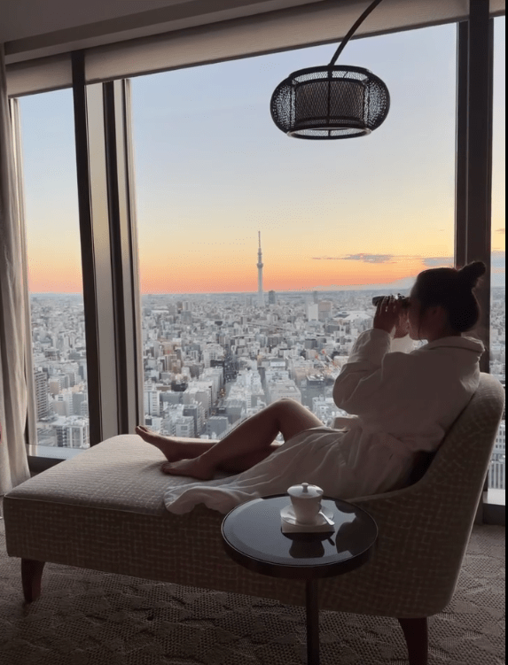 黃碧蓮在酒店房間穿浴袍,手持望遠鏡欣賞東京景色。