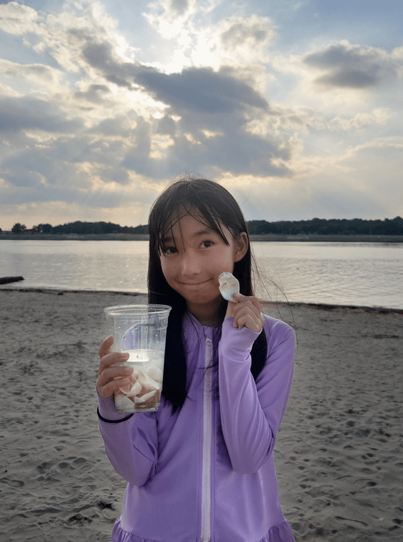 平田琉七在沙灘上展示收集到的貝殼,笑意盈盈。