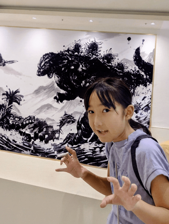 平田琉七在哥斯拉水墨壁畫前學怪獸動作,神情靈動。