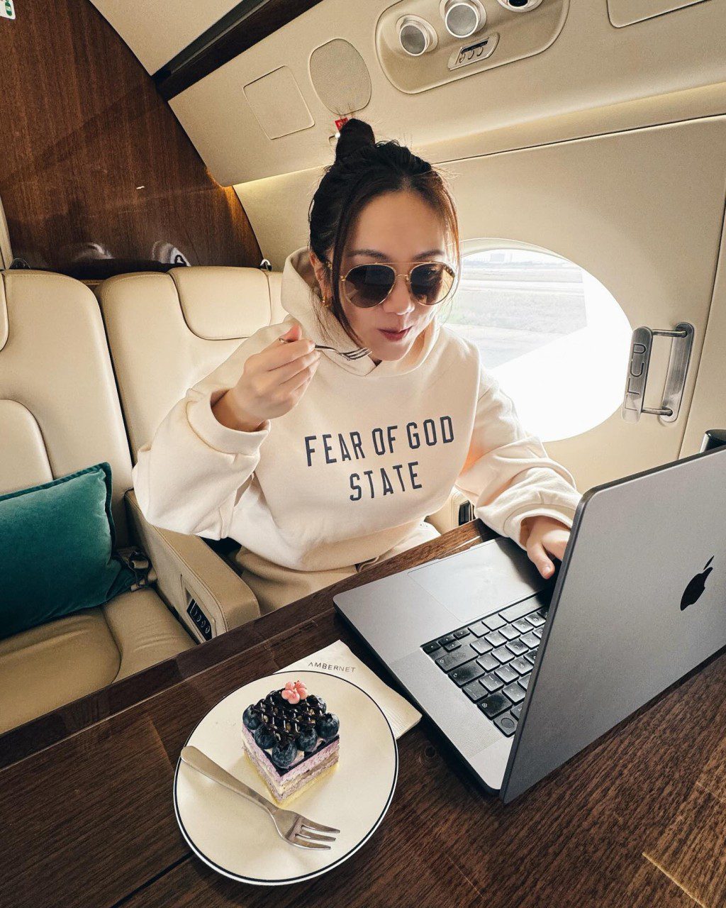 G.E.M.坐在私人飛機內，一邊吃蛋糕一邊對着電腦工作。