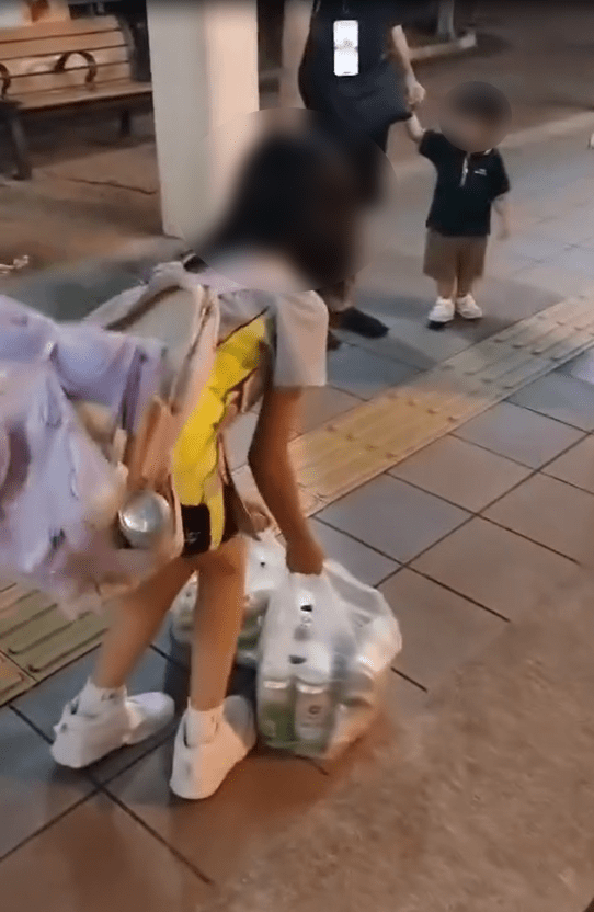 因物品太重,女童不時要放下膠袋休息,也跟不上前方父親的步伐。