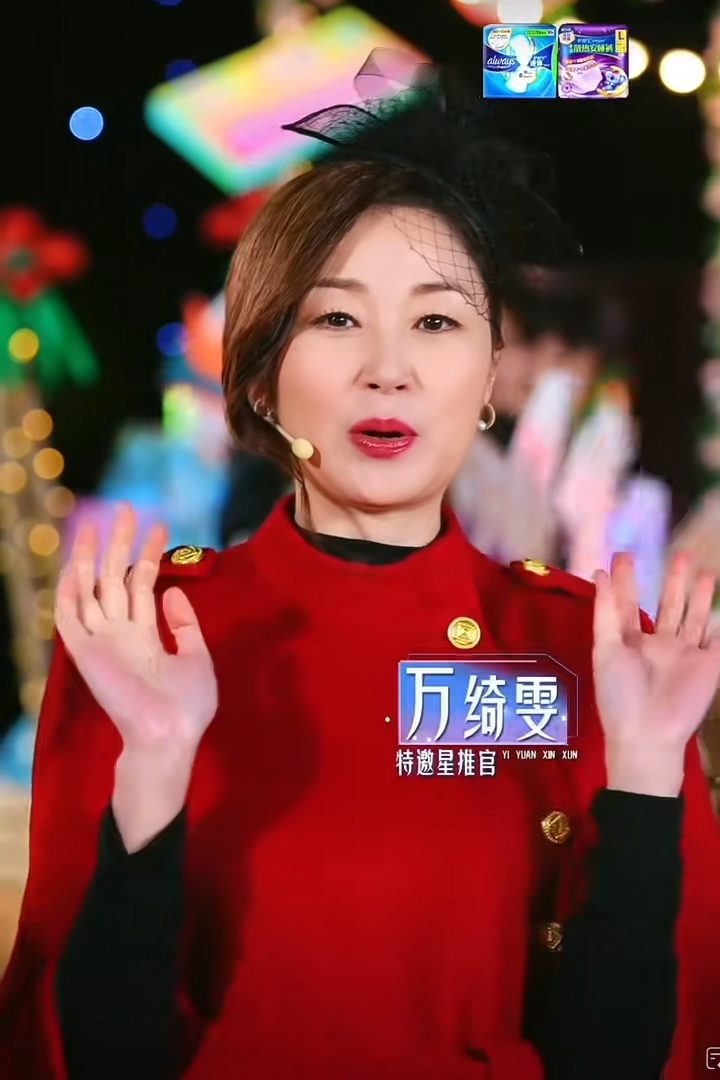 萬綺雯頭戴黑色禮帽,身穿紅色高領斗篷外套。