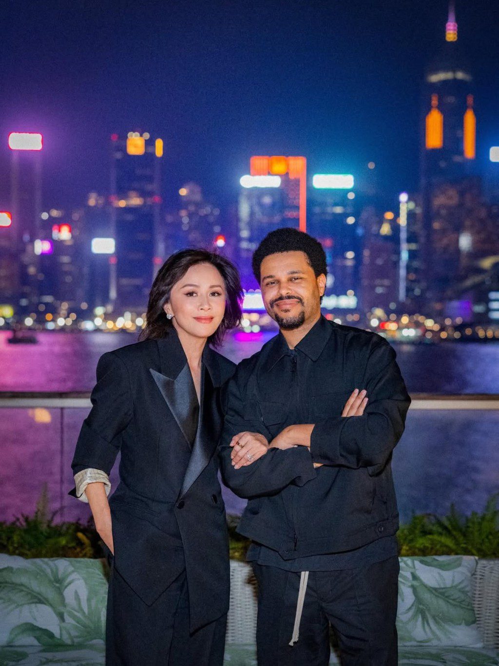 劉嘉玲以一身黑色西裝造型與 The Weeknd 合照,身後的維港夜景璀璨奪目。